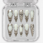 Set de dix press-on nails longs blanc laiteux et argent, avec ornements métalliques dans leur boîte.