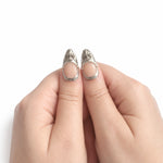 Nude & Argent — Amande : press-on nails portés, détail des pouces, ornements argentés sur fond blanc.