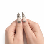 Blanc & Argent — Long : press-on nails portés, détail des pouces, ornements argentés sur fond blanc.