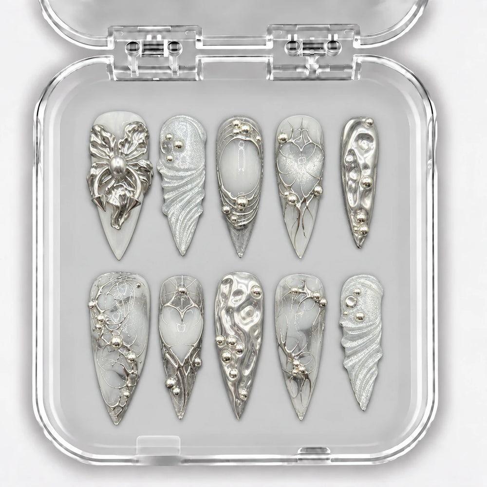 Ongles press-on NELI argentés et blancs avec ornements en relief, présentés dans une boîte transparente.
