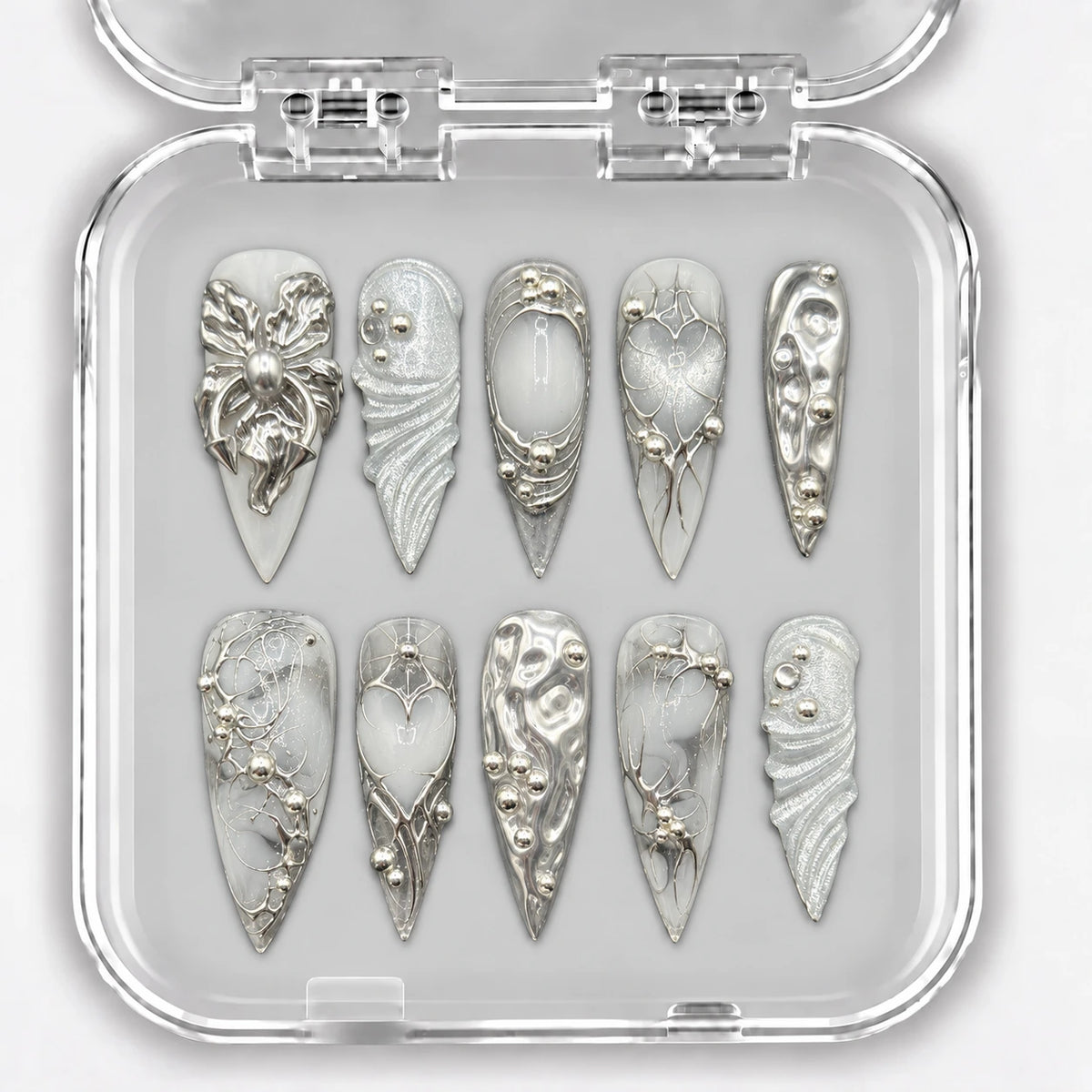 Ongles press-on NELI argentés et blancs avec ornements en relief, présentés dans une boîte transparente.
