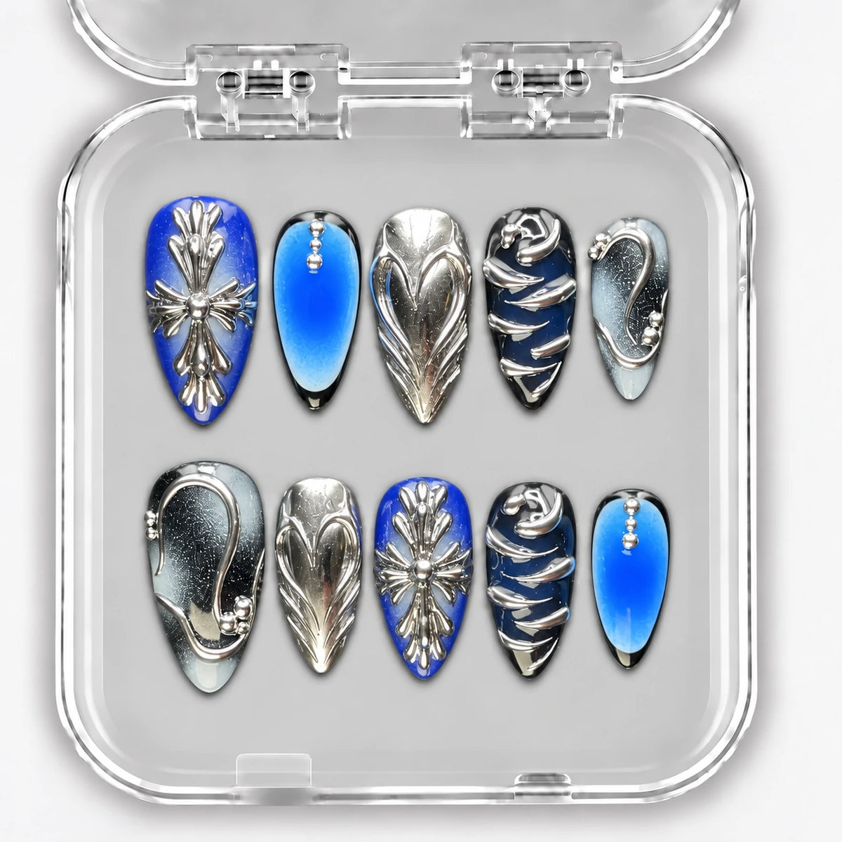 Ongles press-on NELI bleus et argentés avec croix et reliefs métalliques, dans une boîte transparente.
